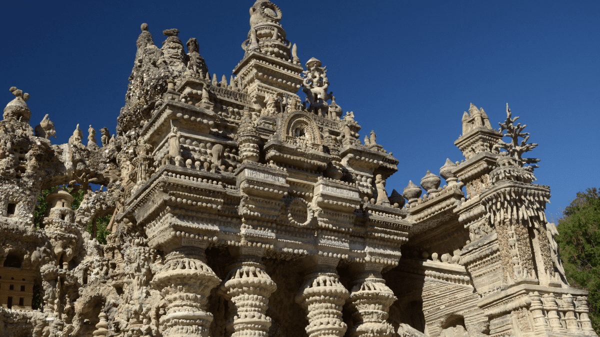 Castelo construído à mão por Ferdinand Cheval ao fundo, com flores amarelas em destaque.