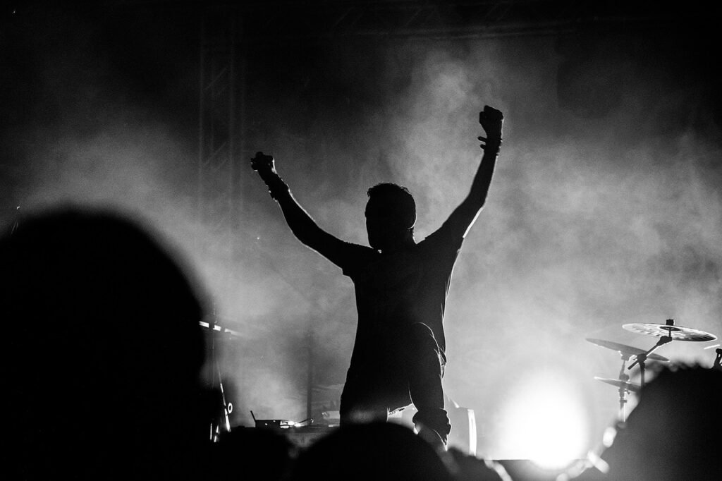 Vocalista com os braços erguidos no palco em meio à fumaça
