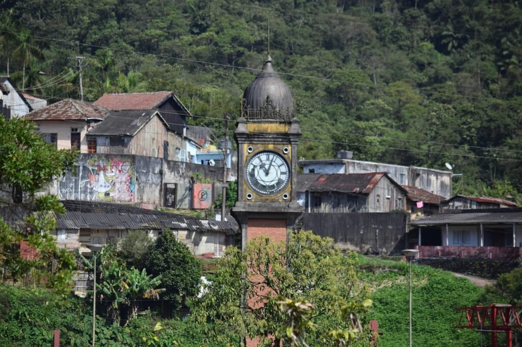 Torre do relógio de Paranapiacaba ao fundo de casas simples e vegetação serrana, símbolo do vilarejo histórico.