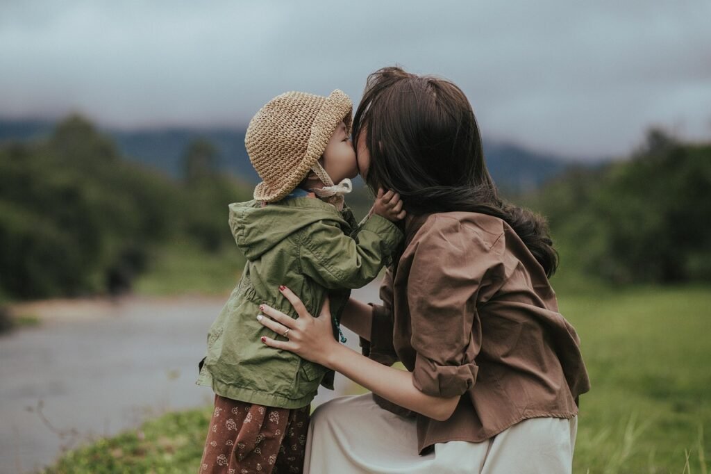 Criança com chapéu beijando a mãe em cenário natural