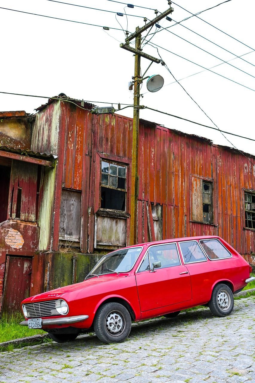 Carro antigo estacionado em rua de paralelepípedo diante de casa de madeira desgastada em Paranapiacaba, remetendo aos anos 50.