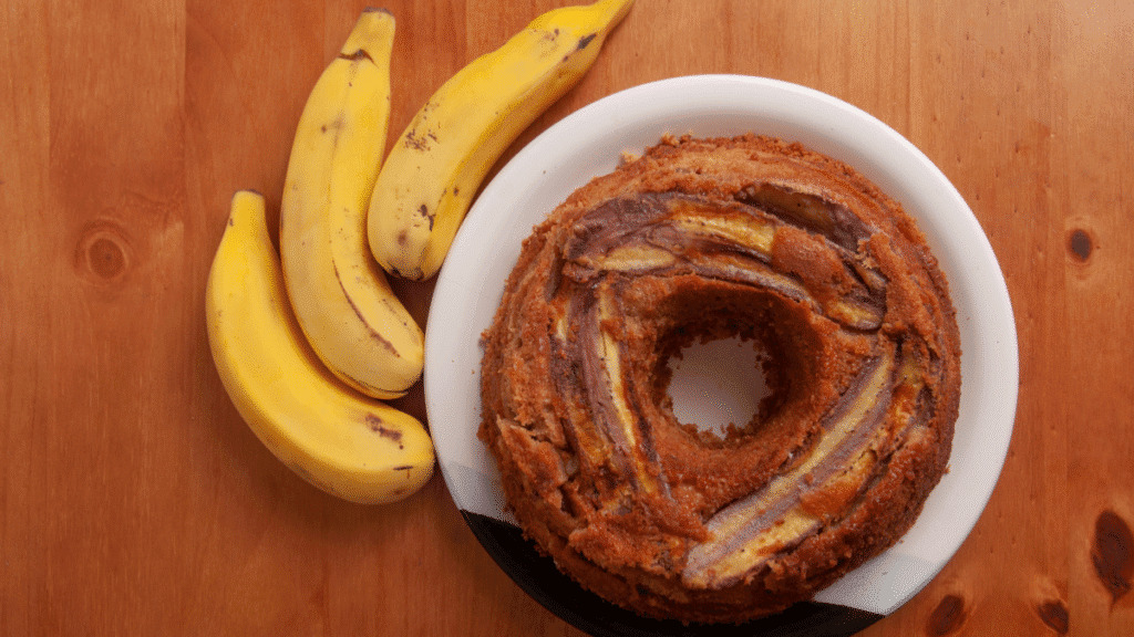 Bolo de banana assado em forma de anel ao lado de bananas frescas