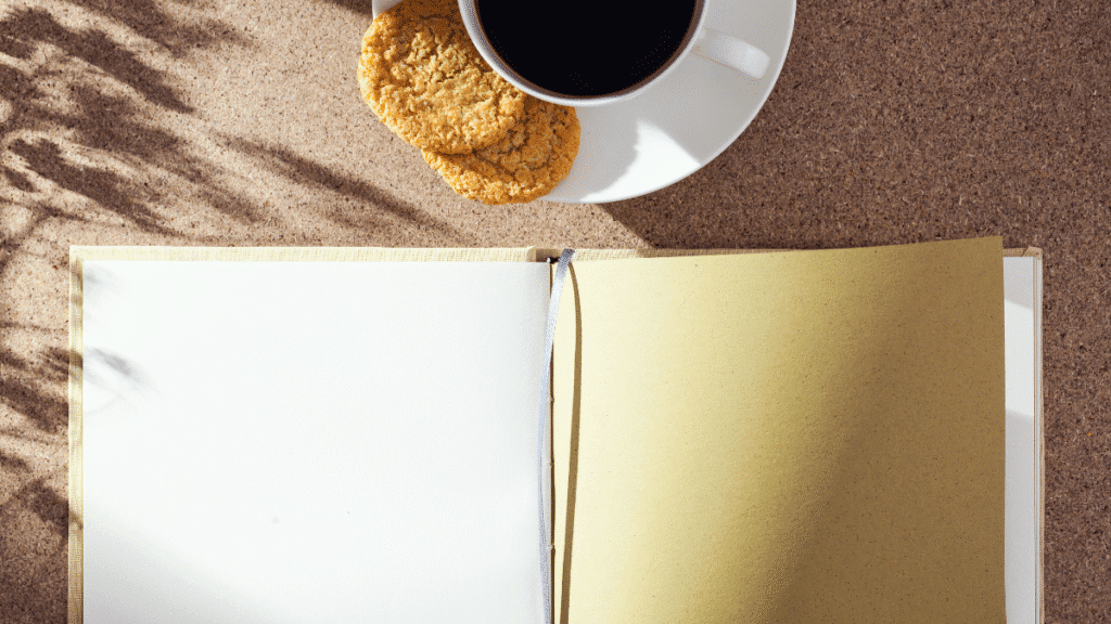 Caderno em branco ao lado de uma xícara de café e biscoitos