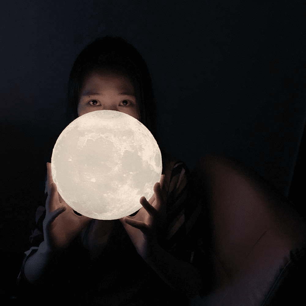 Pessoa segurando luminária lua 3D acesa no escuro, com efeito realista e mágico